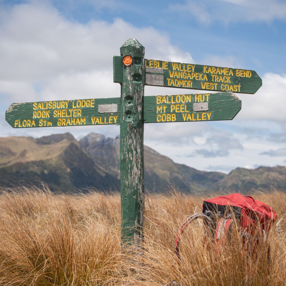 A weathered green track signpost in New Zealand tussock country